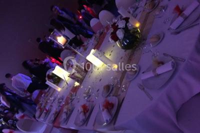 Miniature Location salle Saint-Maximin (Oise) - L'Art d'Oise #27 Salle décorée pour un événement, avec des tables rondes dressées, chaises rouges et un fond floral rose.