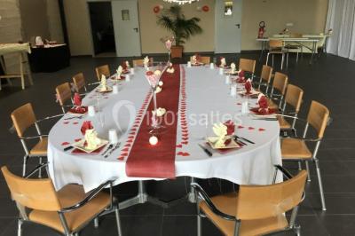 Miniature Location salle Saint-Maximin (Oise) - L'Art d'Oise #28 Salle décorée pour un événement, avec des tables rondes dressées, chaises rouges et un fond floral rose.