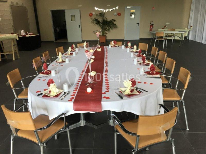 Table décorée pour un événement, nappée de blanc avec un chemin de table rouge, entourée de chaises en bois.