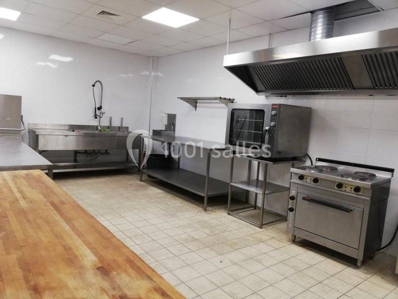 Cuisine professionnelle avec plan de travail en bois, évier inox, four, plaques de cuisson et hotte d'extraction.