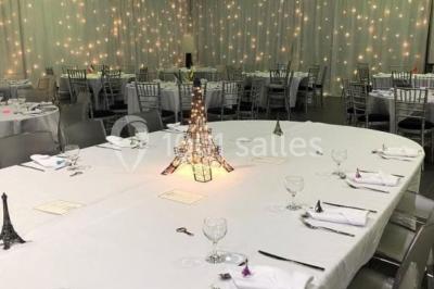 Miniature Location salle Saint-Maximin (Oise) - L'Art d'Oise #17 Salle décorée pour un événement, avec des tables rondes dressées, chaises rouges et un fond floral rose.