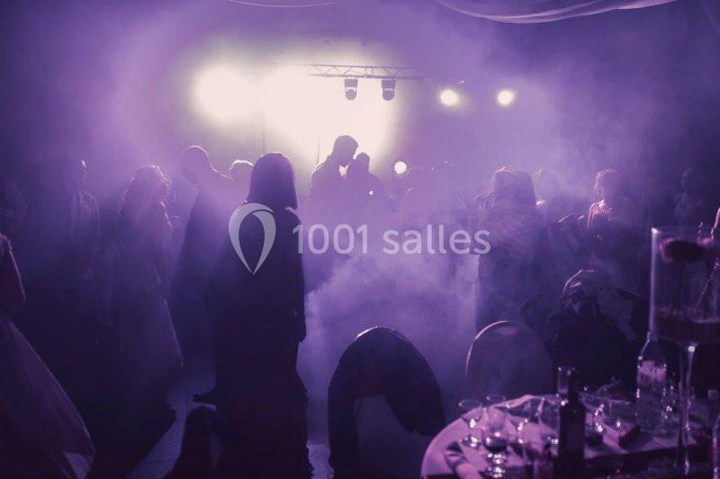 Des personnes dansent dans une ambiance tamisée avec des lumières vives et de la fumée sur une piste de soirée.
