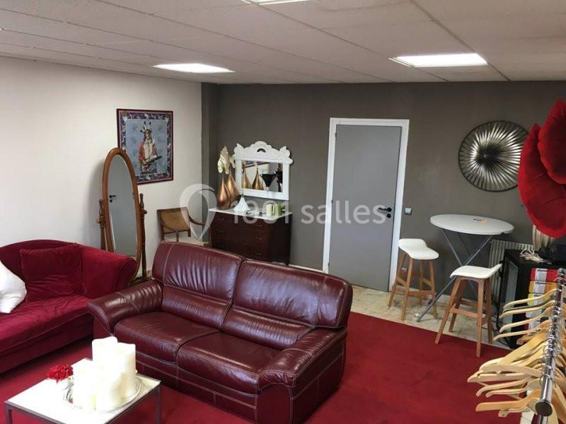 Salon aménagé avec canapés rouges, miroir sur pied, commode, table haute avec tabourets et décorations murales.