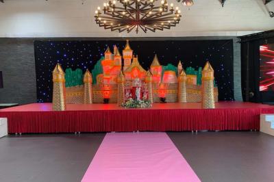 Miniature Location salle Saint-Maximin (Oise) - L'Art d'Oise #14 Salle décorée pour un événement, avec des tables rondes dressées, chaises rouges et un fond floral rose.