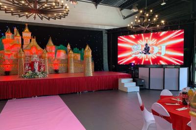 Miniature Location salle Saint-Maximin (Oise) - L'Art d'Oise #11 Salle décorée pour un événement, avec des tables rondes dressées, chaises rouges et un fond floral rose.