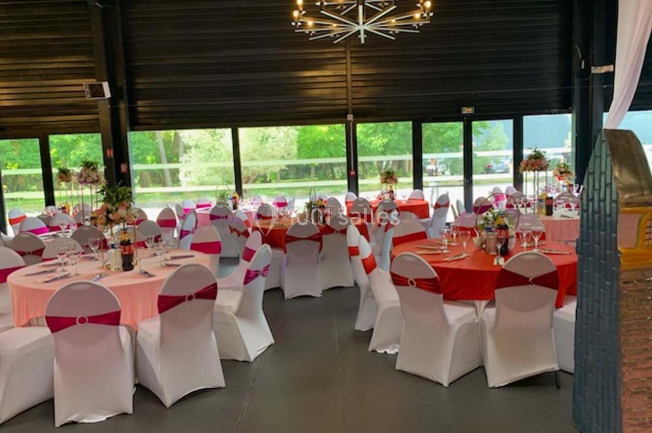 Salle de réception décorée avec des tables rondes, nappes colorées et chaises blanches, éclairée par un lustre moderne.
