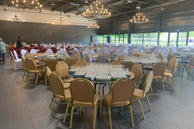 Miniature Location salle Saint-Maximin (Oise) - L'Art d'Oise #7 Salle décorée pour un événement, avec des tables rondes dressées, chaises rouges et un fond floral rose.