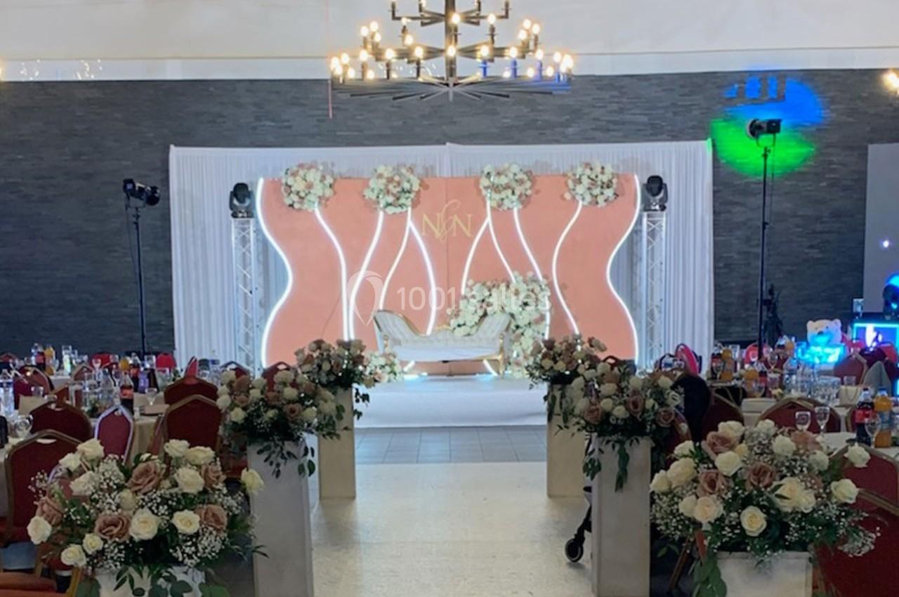 Salle de réception décorée avec des fleurs, un canapé central et un éclairage chaleureux sous un lustre imposant.