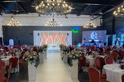 Miniature Location salle Saint-Maximin (Oise) - L'Art d'Oise #9 Salle décorée pour un événement, avec des tables rondes dressées, chaises rouges et un fond floral rose.