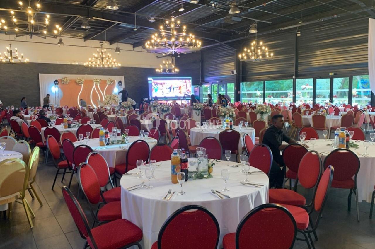 Salle de réception décorée avec des tables rondes dressées, chaises rouges et éclairage suspendu.