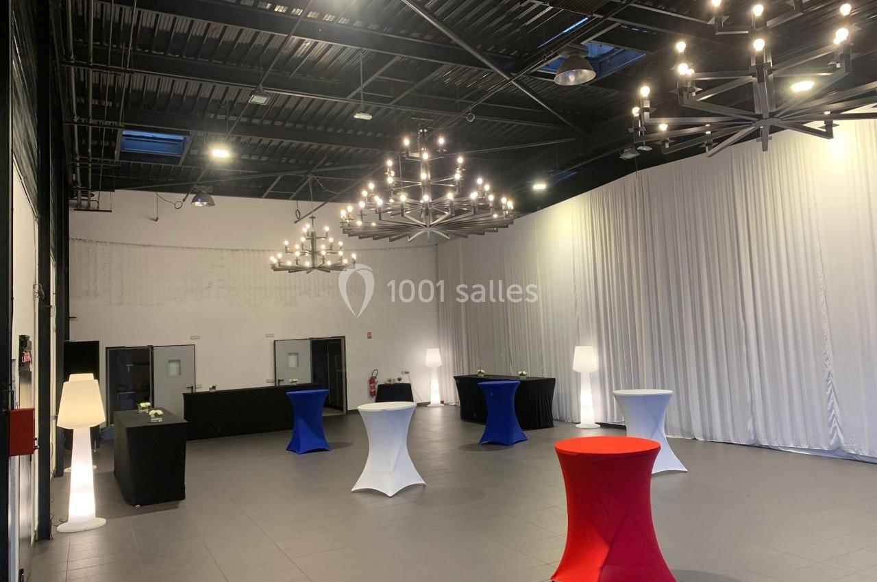 Salle de réception moderne avec tables hautes colorées, rideaux blancs, lustres suspendus et éclairage tamisé.