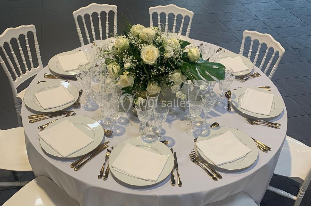 Table ronde élégamment dressée avec vaisselle blanche, couverts dorés et centre de table floral composé de roses blanches.