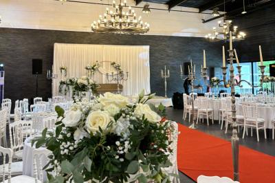 Miniature Location salle Saint-Maximin (Oise) - L'Art d'Oise #3 Salle décorée pour un événement, avec des tables rondes dressées, chaises rouges et un fond floral rose.