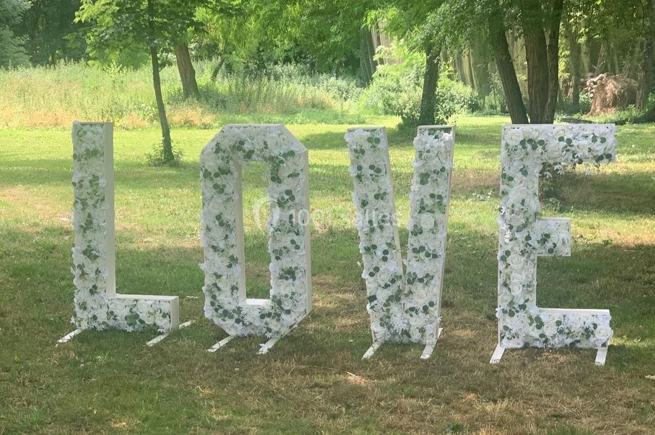 Lettres géantes formant le mot ’LOVE’, décorées de fleurs blanches, installées dans un parc verdoyant.