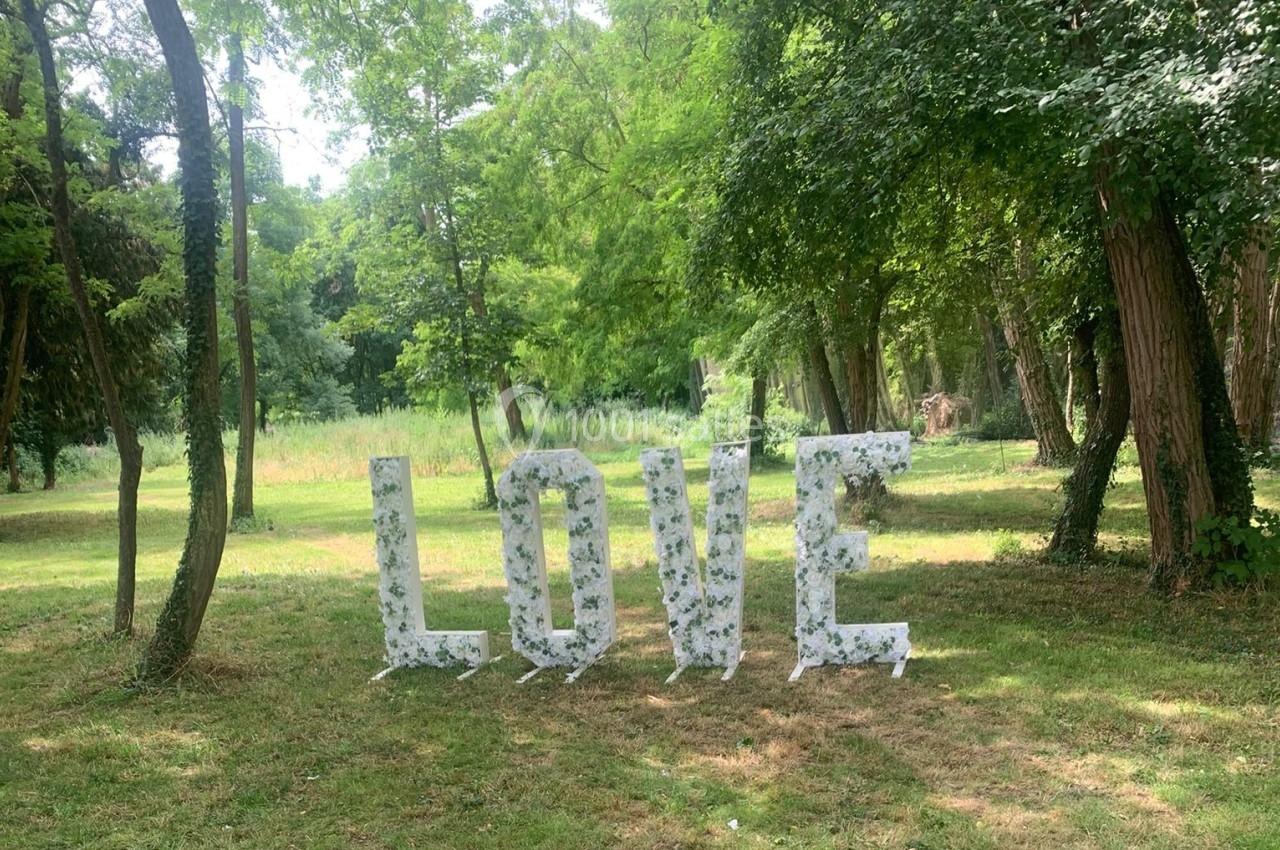 Lettres géantes formant le mot ’LOVE’, décorées de fleurs blanches, placées dans un parc verdoyant.