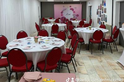 Miniature Location salle Saint-Maximin (Oise) - L'Art d'Oise #42 Salle décorée pour un événement, avec des tables rondes dressées, chaises rouges et un fond floral rose.