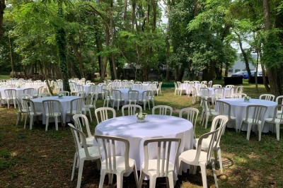 Salle décorée avec des tables rondes, nappes blanches et chaises rouges, prête pour un événement festif.