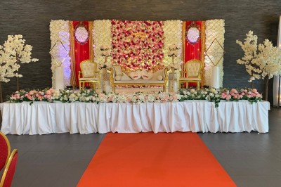 Salle décorée avec des tables rondes, nappes blanches et chaises rouges, prête pour un événement festif.