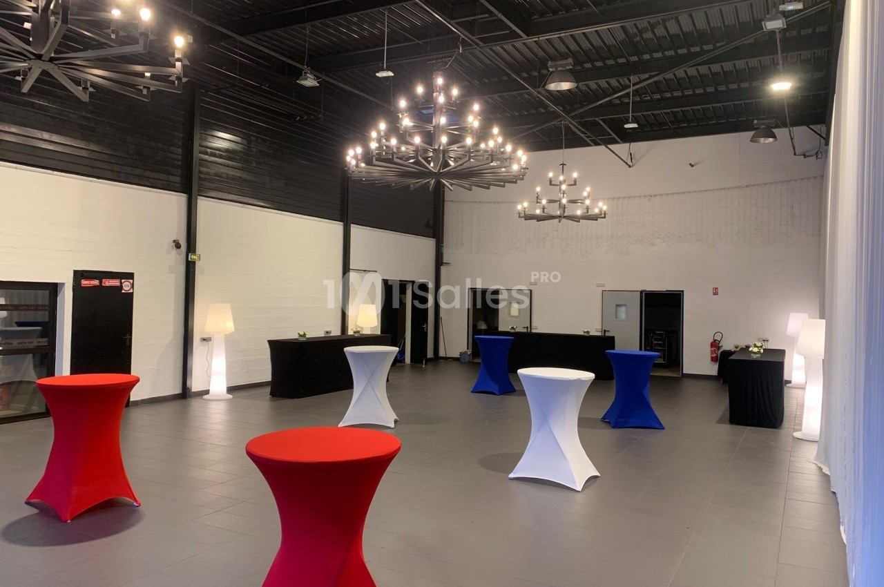 Salle de réception moderne avec tables hautes colorées, lustres suspendus et murs blancs et noirs.