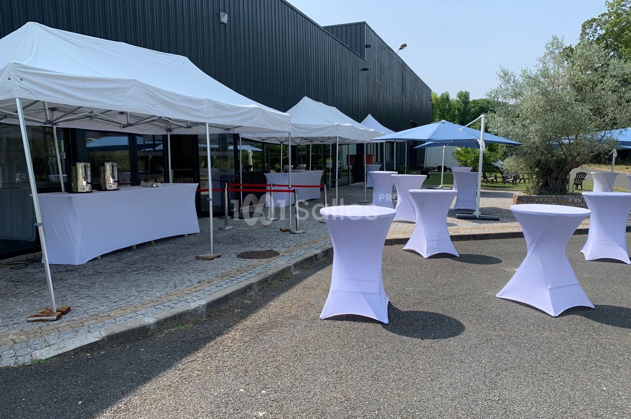 Tentes blanches et tables hautes recouvertes de nappes violettes disposées en extérieur sur un sol pavé.