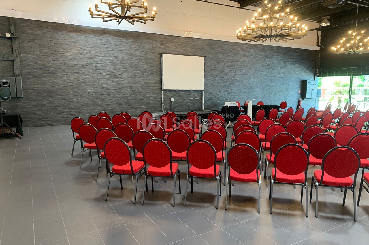 Salle de conférence avec des chaises rouges disposées en arc de cercle face à un écran de projection blanc.