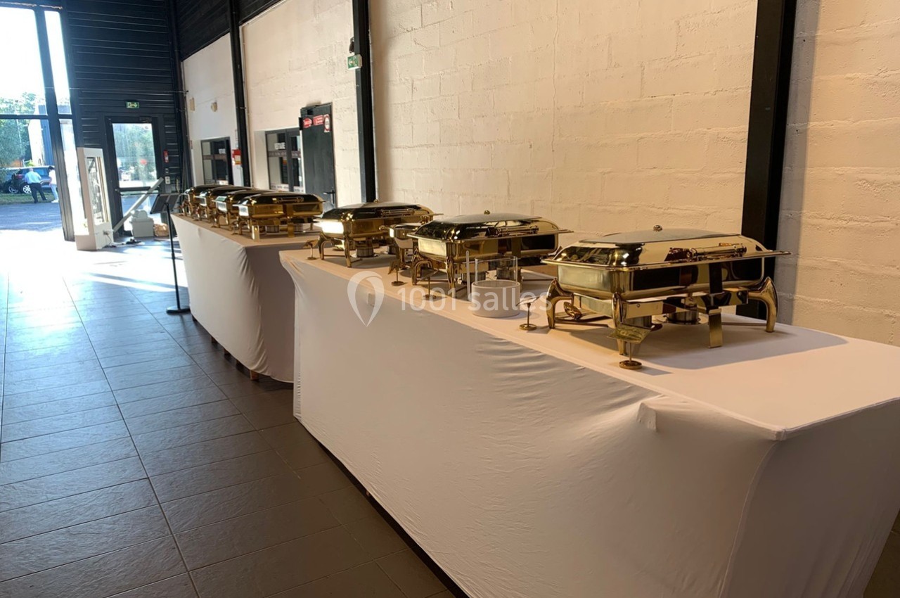 Buffet avec plusieurs plats en chafing dishes dorés alignés sur des tables recouvertes de nappes blanches.