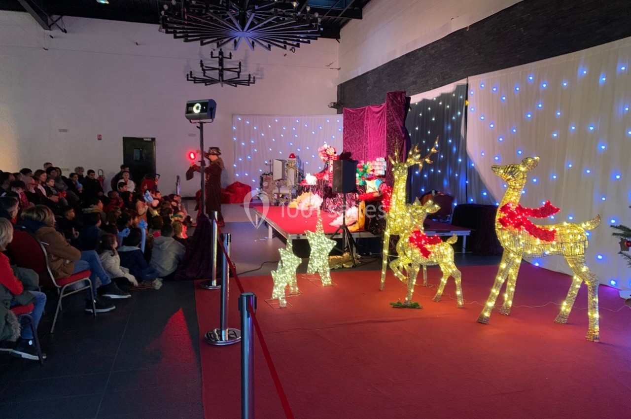 Spectacle de Noël avec un public assis, des décorations lumineuses en forme de rennes et une scène éclairée.