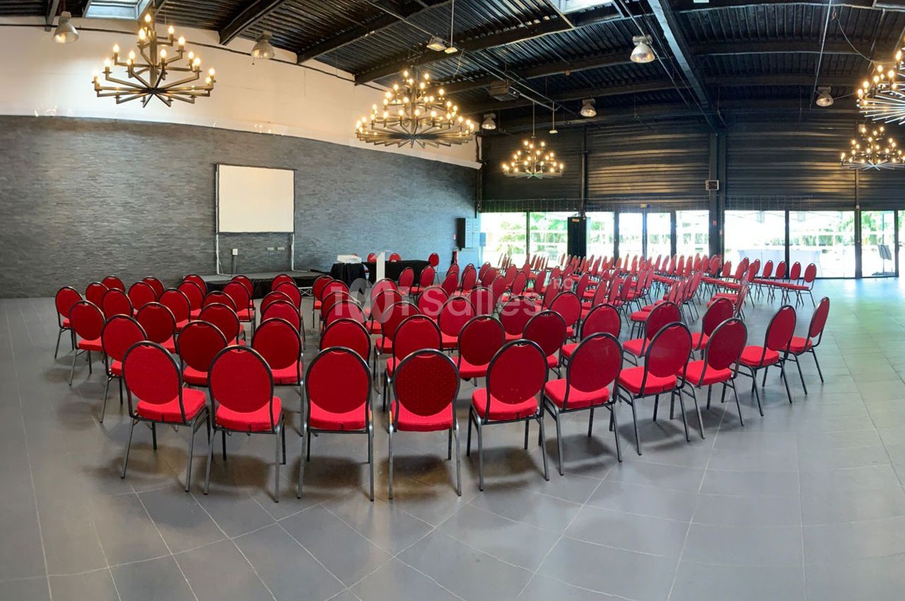 Salle de conférence avec des rangées de chaises rouges disposées en cercle face à un écran de projection.