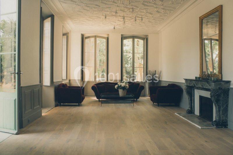 Salon lumineux avec parquet en bois clair, canapés rouges, cheminée en marbre et grandes fenêtres donnant sur un jardin.