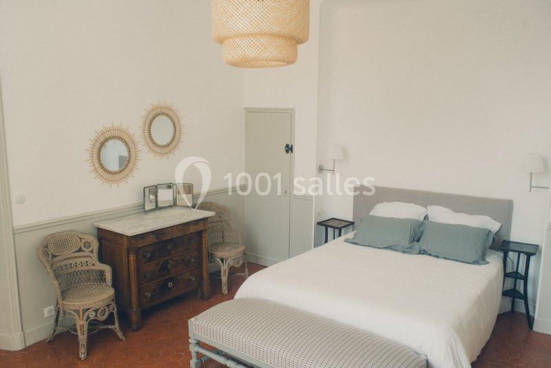 Chambre lumineuse avec lit double, commode en bois, deux miroirs ronds et fauteuils en osier sur un sol en terre cuite.