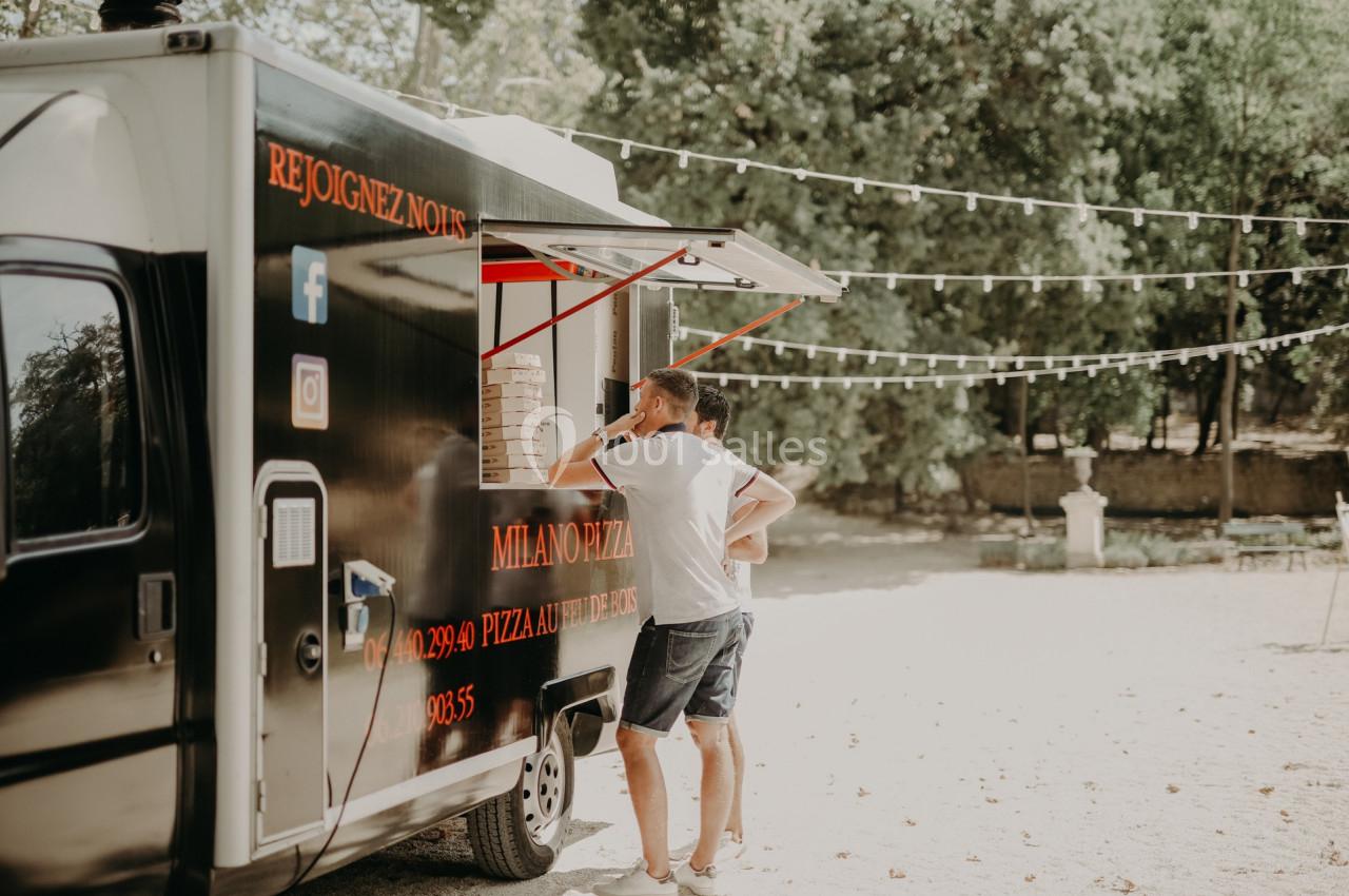 Deux personnes commandent à un food truck noir stationné en extérieur, entouré d'arbres et de guirlandes lumineuses.