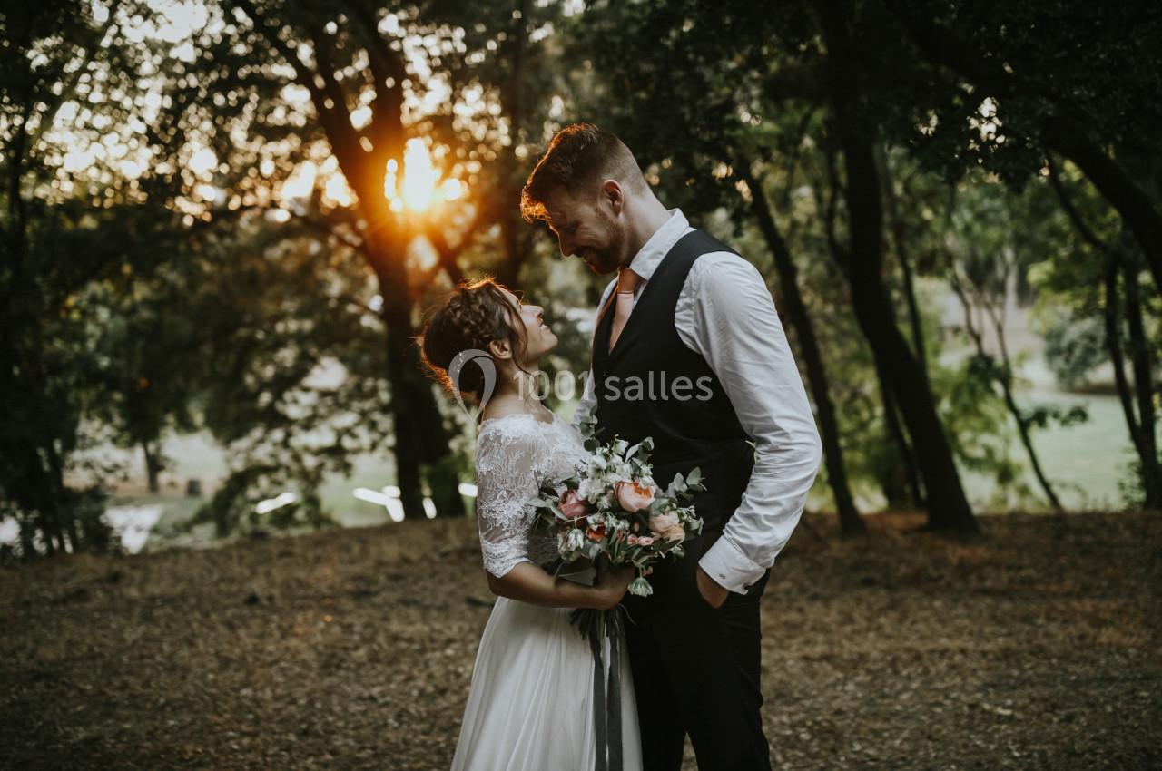 Un couple en tenue de mariage se regarde tendrement dans une forêt au coucher du soleil.