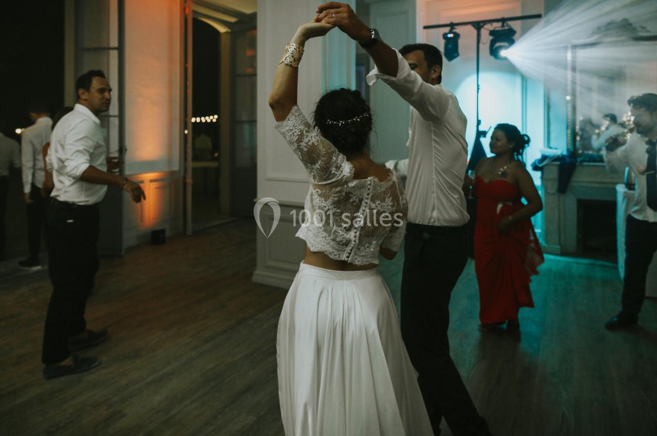 Un couple danse dans une salle éclairée, entouré de quelques invités en tenue de soirée.