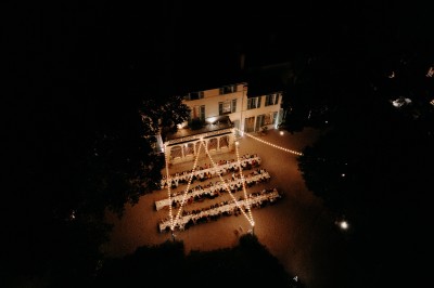 Chaises transparentes disposées en rangées sur une allée blanche, entourées d'arbres dans un cadre extérieur.