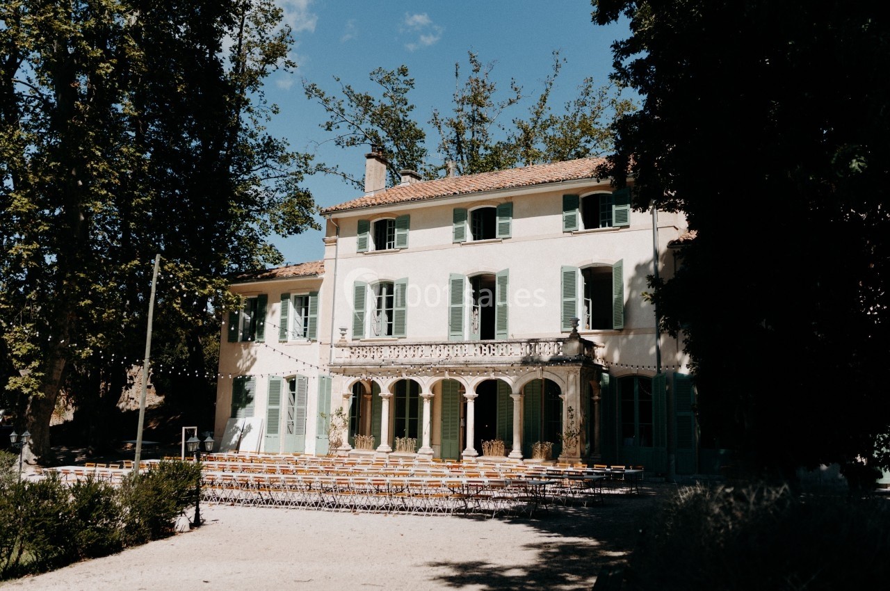 Façade d'une grande maison provençale entourée d'arbres, avec des chaises disposées en extérieur sur une terrasse.