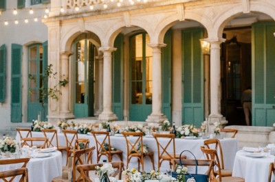 Chaises transparentes disposées en rangées sur une allée blanche, entourées d'arbres dans un cadre extérieur.