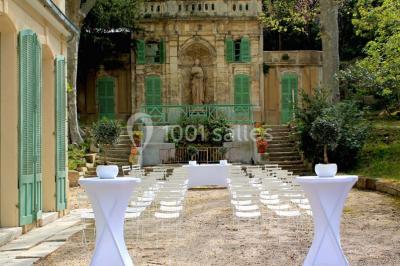 Chaises transparentes disposées en rangées sur une allée blanche, entourées d'arbres dans un cadre extérieur.