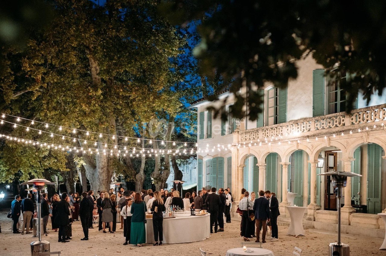 Groupe de personnes rassemblées en soirée dans une cour éclairée par des guirlandes lumineuses, devant un bâtiment ancien.
