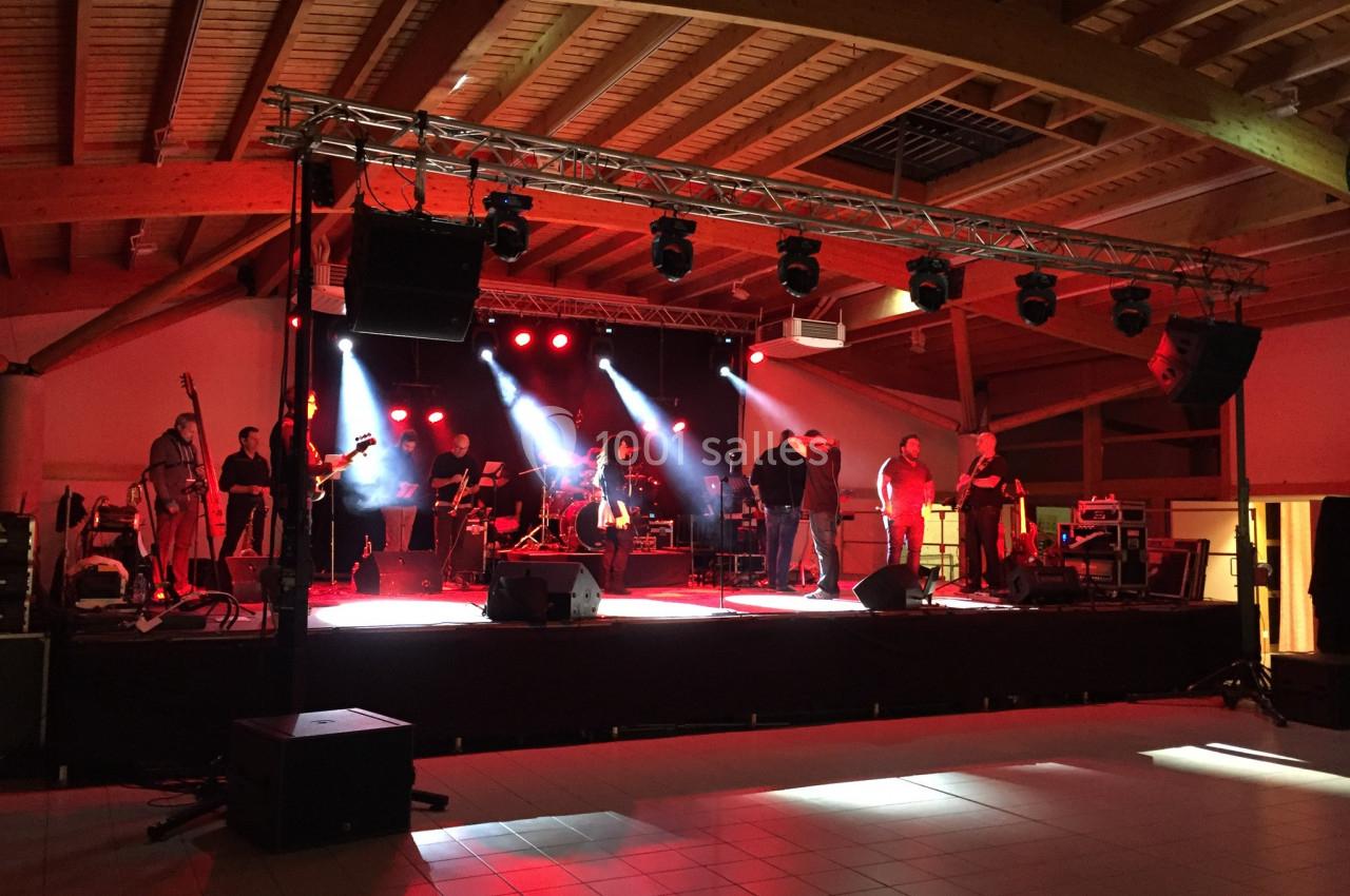 Groupe de musiciens sur une scène éclairée par des projecteurs rouges dans une salle avec charpente en bois.