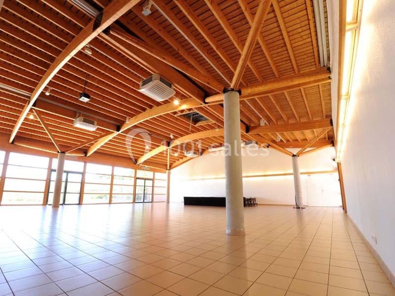 Salle spacieuse avec plafond en bois, grandes baies vitrées, carrelage beige et éclairage intégré.