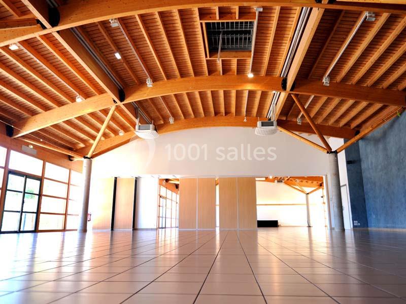 Grande salle lumineuse avec plafond en bois, carrelage au sol, murs clairs et grandes ouvertures vitrées.