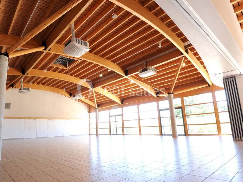 Grande salle lumineuse avec plafond en bois, baies vitrées et carrelage clair, adaptée pour événements ou réunions.