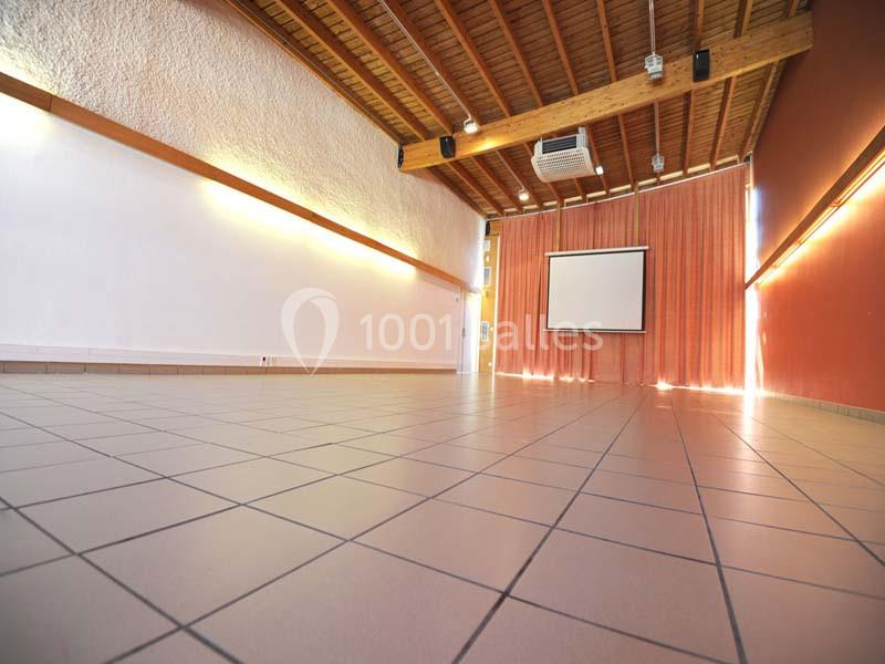 Salle vide avec sol carrelé, murs blancs et rouges, plafond en bois, rideaux fermés et écran de projection.