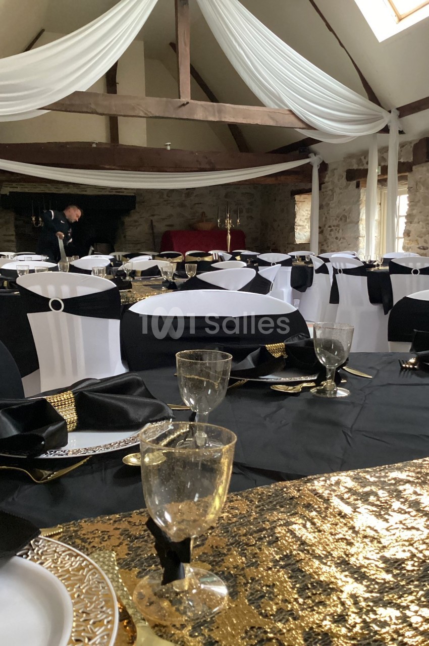 Salle de réception décorée avec des tables dressées en noir, blanc et or, sous un plafond avec drapés blancs.