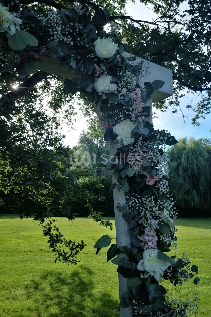 Arche en bois décorée de fleurs blanches et roses avec feuillage, installée dans un jardin verdoyant.