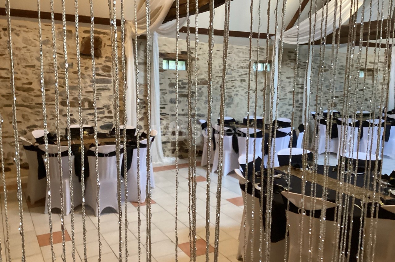 Salle de réception décorée avec des tables rondes habillées de nappes blanches et noires, vue à travers des guirlandes.