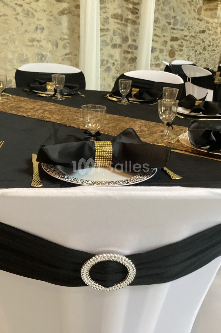 Table décorée avec une nappe noire et blanche, ornée de nœuds noirs, détails dorés et vaisselle élégante.
