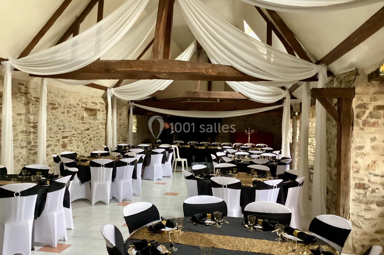 Salle de réception avec poutres apparentes, tables rondes décorées en noir et blanc et nappes dorées.