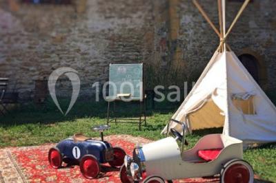 Scooter rose décoré de fleurs roses et blanches, stationné près d'un mur en pierre et d'une porte en bois.