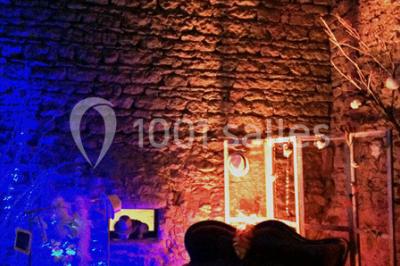 Scooter rose décoré de fleurs roses et blanches, stationné près d'un mur en pierre et d'une porte en bois.